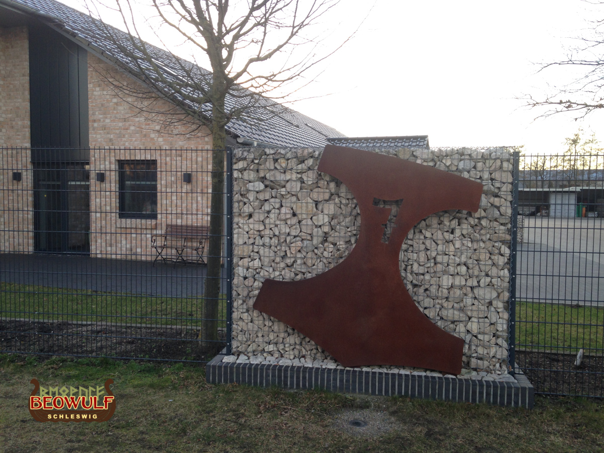 Mannshoher Thorhammer aus Metall an einer Mauer vor einem Haus, um die Hausnummer 7 zu kennzeichnen.