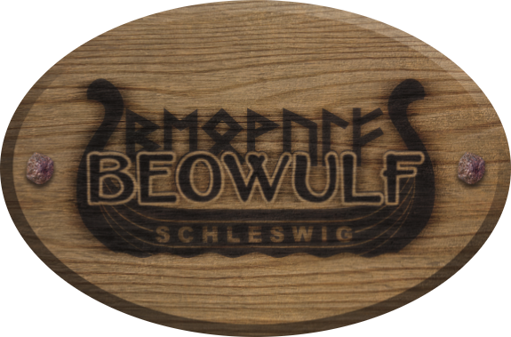 Holztafel mit eingebranntem Logo von Beowulf Schleswig, das ein aus Planken bestehendes Schiff mit geschwungenen Steven darstellt und mittig den Namen Beowulf sowohl normal als auch in Runenschrift zeigt.